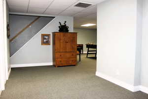 Finished below grade area with carpet, baseboards, a paneled ceiling, and stairway