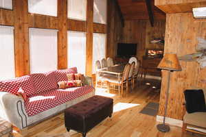 Living area with wooden walls, beam ceiling, wooden ceiling, wood-type flooring, and high vaulted ceiling