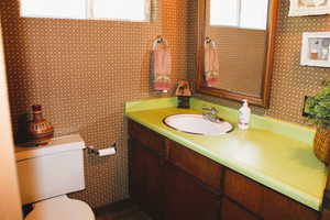 Bathroom with toilet, vanity, and wallpapered walls