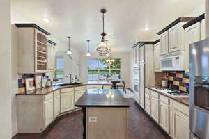 Kitchen featuring a sink, a peninsula, white appliances, backsplash, and a kitchen island