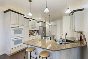 Kitchen featuring a peninsula, a breakfast bar area, a sink, white appliances, and decorative backsplash