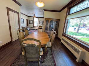 Dining room featuring radiator heating unit, crown molding, dark wood-type flooring, baseboards, and a ceiling fan