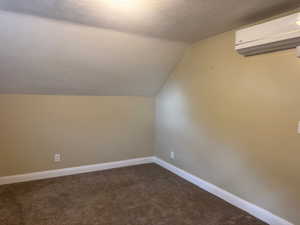 Additional living space featuring a wall mounted air conditioner, lofted ceiling, carpet floors, baseboards, and a textured ceiling