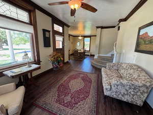 Living room with ornamental molding, wood finished floors, stairs, a ceiling fan, and baseboards