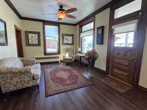 Living room featuring radiator heating unit, ornamental molding, wood finished floors, baseboards, and ceiling fan