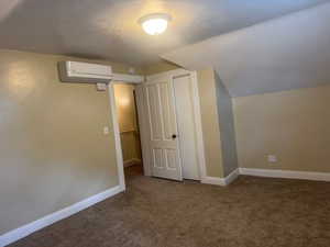 Bonus room featuring a wall unit AC, carpet flooring, baseboards, a textured ceiling, and vaulted ceiling