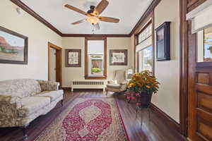Living room with radiator, baseboards, wood finished floors, ceiling fan, and crown molding