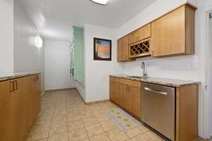 Kitchen with dishwasher, a sink, light stone countertops, and tasteful backsplash