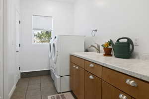 Clothes washing area featuring separate washer and dryer, tile patterned flooring, baseboards, and cabinet space