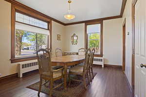 Dining room featuring crown molding, baseboards, plenty of natural light, dark wood-style floors, and radiator heating unit