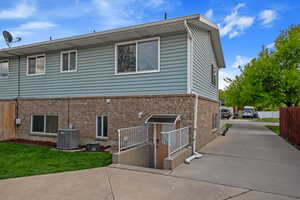 Rear view of property with central AC unit, fence, brick siding, and driveway