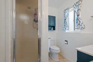 Full bath with toilet, a stall shower, vanity, and baseboards