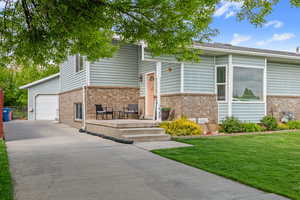 Raised ranch with brick siding, driveway, a front lawn, and an attached garage