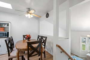 Dining room with a skylight, ceiling fan, and light wood-style flooring