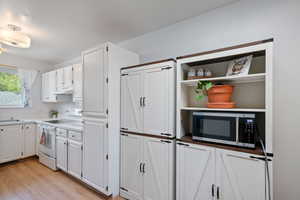 Kitchen featuring white electric range, stainless steel microwave, white cabinets, and a sink