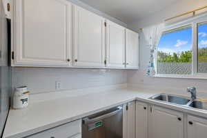Kitchen with dishwasher, a sink, backsplash, and white cabinets