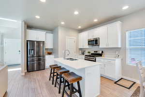 Kitchen with appliances with stainless steel finishes, a sink, light LVP flooring, white cabinetry, and a center island with sink