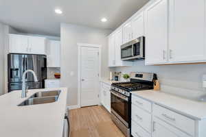 Kitchen with appliances with stainless steel finishes, a sink, light LVP flooring, white cabinetry, and a center island with sink