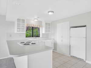 Kitchen featuring white appliances, a sink, a peninsula, light countertops, and glass insert cabinets