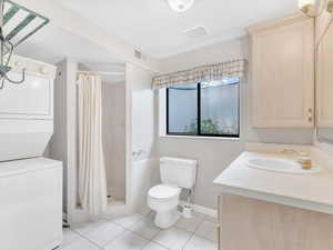 Full bath featuring estacked washer and dryer, tile patterned flooring, toilet, and a shower stall