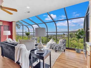 Living area with a sunroom, a ceiling fan, plenty of natural light, wood finished floors, and expansive windows