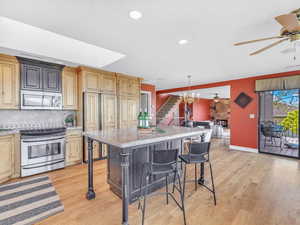 Kitchen with appliances with stainless steel finishes, a ceiling fan, a breakfast bar area, light wood-style flooring, and recessed lighting