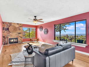 Living area with a ceiling fan, wood finished floors, a textured ceiling, a fireplace, and baseboards