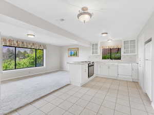 Kitchen featuring dishwasher, light colored carpet, glass insert cabinets, a peninsula, and light tile patterned flooring