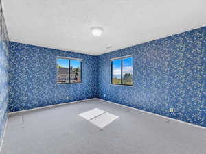 Carpeted empty room featuring wallpapered walls and a textured ceiling