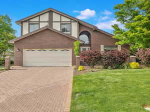 View of front of house featuring decorative driveway, brick siding, and a garage