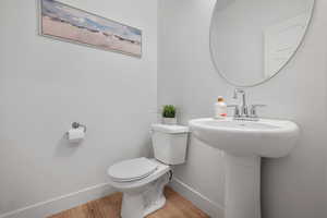 Half bathroom with baseboards, toilet, and wood finished floors
