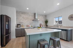 Kitchen with fridge with ice dispenser, stainless steel dishwasher, wall chimney range hood, a sink, and light wood finished floors