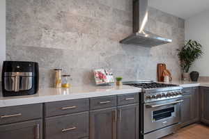 Kitchen with wall chimney exhaust hood, high end range, light countertops, and light wood-style floors