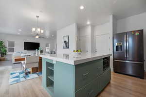 Kitchen featuring stainless steel fridge, light wood-style flooring, a chandelier, a center island, and light countertops