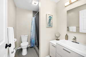 Full bathroom with toilet, a tiled shower with curtain, vanity, and baseboards