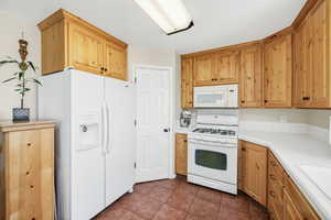 Kitchen featuring white appliances, tile counters, dark tile patterned flooring, and a sink