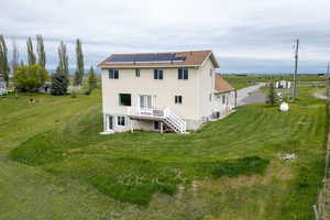 Back of house featuring solar panels, a deck, stairway, a yard, and a shingled roof
