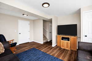 Basement Living room featuring dark wood-style flooring, stairs, and baseboards