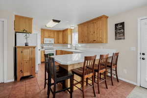 Kitchen with white appliances, a peninsula, tile counters, and light tile patterned floors