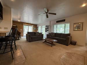 Living room featuring wooden walls, carpet floors, a ceiling fan, and a textured ceiling