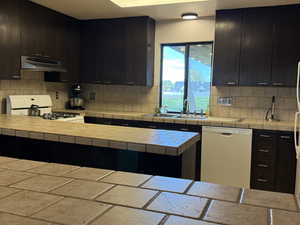 Kitchen with under cabinet range hood, white appliances, a sink, and backsplash