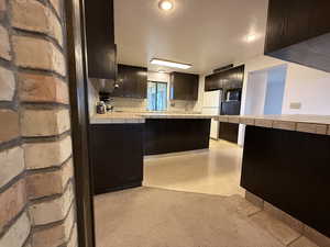 Kitchen featuring tile countertops, built in microwave, freestanding refrigerator, decorative backsplash, and a peninsula