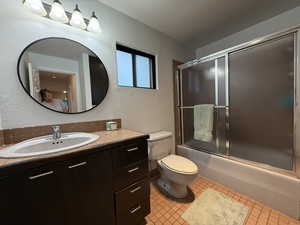 Full bath featuring a textured wall, bath / shower combo with glass door, vanity, toilet, and tile patterned floors
