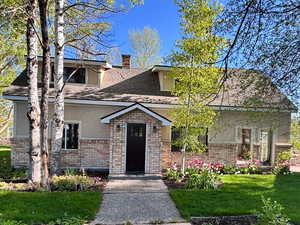 View of front of home featuring a front yard, stucco siding, a chimney, and a shingled roof
