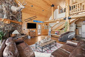 Living area with high vaulted ceiling, log walls, wood-type flooring, stairs, and wooden ceiling