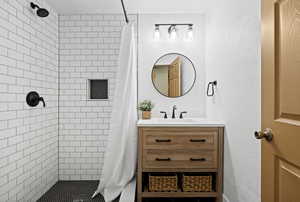Full bath featuring tiled shower, vanity, and a textured wall