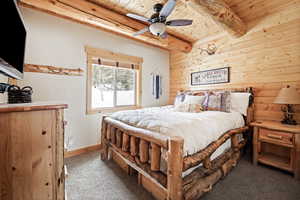 Carpeted bedroom with wooden ceiling, beam ceiling, wooden walls, baseboards, and ceiling fan