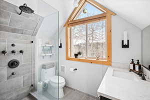 Full bathroom featuring vaulted ceiling, a tile shower, toilet, vanity, and baseboards