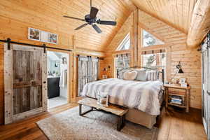 Bedroom featuring a barn door, wooden ceiling, hardwood / wood-style floors, wooden walls, and high vaulted ceiling