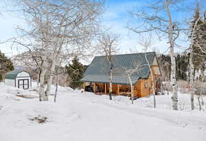 Snow covered property featuring metal roof, a storage unit, and an outbuilding